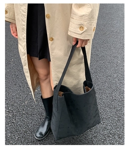 Scatto urbano di una borsa tote grande nera opaca abbinata a un elegante trench coat