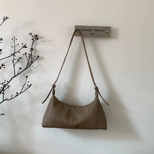 Detail of a brown textured leather shoulder bag with adjustable strap and metal logo