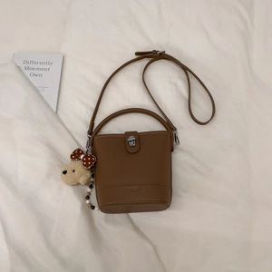 Detail view of brown bucket bag featuring a silver twist lock and plush puppy charm accessory