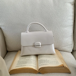 Chic cream leather square handbag placed on a book for a minimalist aesthetic style