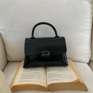Detail of a sleek black patent leather square handbag with metal buckle on vintage books