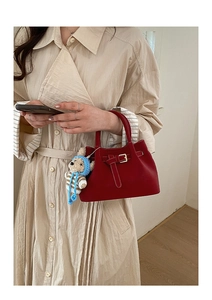 Close-up of a burgundy suede bucket bag with a cute knitted bear charm on handle