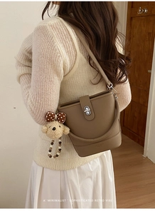 Detail view of brown pebbled leather bucket bag with silver twist lock and bear charm