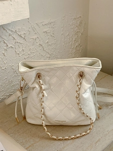Elegant white quilted crossbody bag with gold chain strap on artistic stone background
