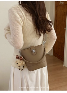 Detailed back view of a brown pebbled leather bucket bag with a cute bear plush charm