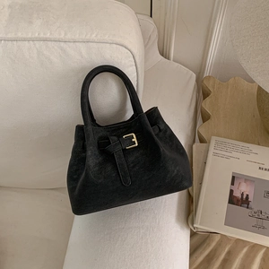 Close-up of black bucket bag with gold square buckle and matte texture on a white sofa