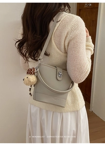 Minimalist grey leather bucket bag with a cute bear pendant on a neutral outfit