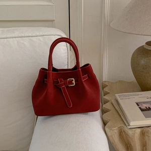 Detail shot of a dark red suede bucket bag with a belt buckle on a stylish sofa