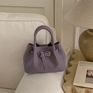 Detail of a purple bucket bag with gold clasp on a beige fabric sofa background