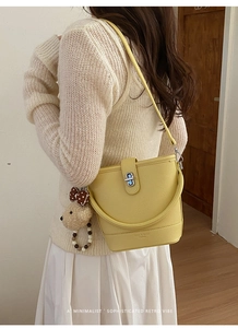 Detail of yellow lychee pattern bucket bag with bear charm and silver lock on a shoulder strap