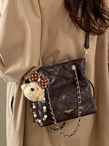 Deep brown quilted crossbody bucket bag with gold chain and plush bear charm detail