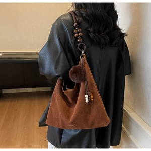 Detail of a dark brown suede tote bag featuring a wooden bead strap and pompom charm