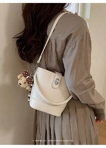Detail view of cream bucket bag featuring lychee texture and cute brown plush bear charm