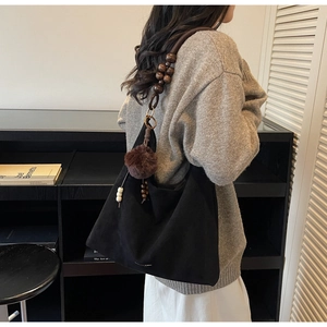 Detail of black matte tote bag featuring wooden bead strap and brown pompom charm detail
