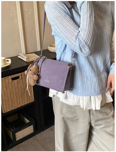 Détail du sac bandoulière violet mat avec logo doré, rivets et breloque ours marron