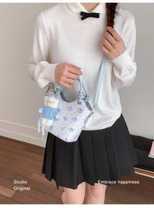 Detail of light blue crossbody bag featuring embossed bear patterns and a plush charm