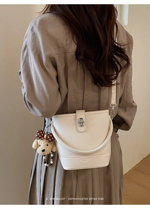 Close-up of white pebble leather bucket bag with silver lock and plush dog charm detail