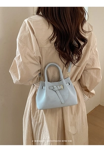 Pale blue matte leather bucket bag with belt knot detail worn by a model in beige