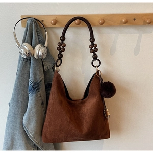 Detail of brown suede tote bag with wooden bead strap and plush pompom charm
