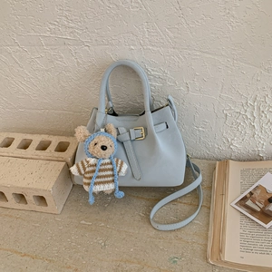 Close-up of a light blue bucket bag with a cute bear charm and golden buckle hardware