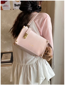 Détail du sac baguette en cuir rose avec logo doré, fermoir et breloque ours en peluche