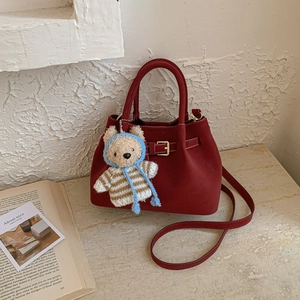 Detail view of burgundy suede bucket bag featuring a cute teddy bear charm accessory