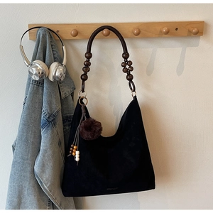 Detail of black suede tote bag featuring unique dark wooden bead strap and fuzzy pompom charm