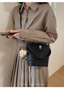 Detail of black pebbled leather bucket bag with silver clasp and plush puppy charm