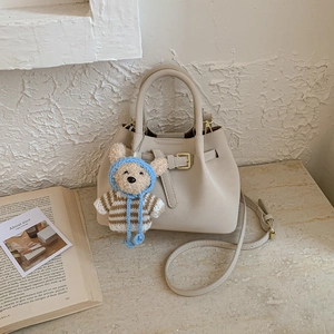 Detail of beige leather bucket bag with gold hardware and a cute teddy bear pendant charm