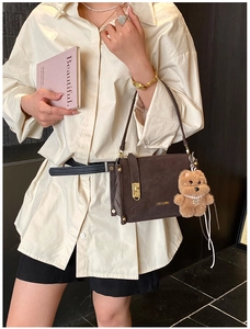 Détail du sac bandoulière marron vintage avec fermoir doré et accessoire de charme d'ours