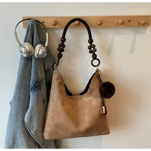 Detail of a brown suede shoulder bag featuring a wooden bead handle and furry charm