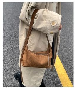 Detailed view of caramel brown suede hobo bag with adjustable strap on beige trench coat