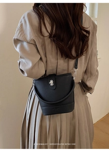 Fashionable black pebble grain bucket bag with silver metal lock on a model's shoulder