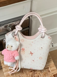 Chic cream bucket bag with pink dessert prints and bear charm on wicker background