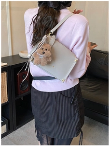 Détail du sac bandoulière en cuir PU gris clair avec logo doré et breloque ours en peluche