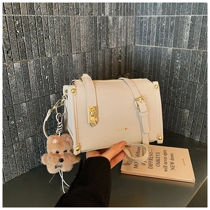 Détail du petit sac carré en cuir crème avec boucle dorée et breloque chien en peluche