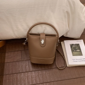 Detail view of brown pebbled leather bucket bag with silver twist lock on dark wood floor