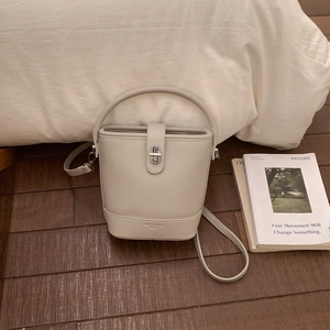 Detail of cream white pebbled leather bucket bag with silver turn-lock and handle