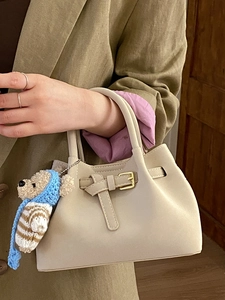 Vintage beige bucket bag with a cute crochet bear charm held by a model in a green blazer