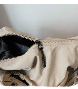 Detail of smooth black zipper with metal slider on a beige nylon crossbody bag