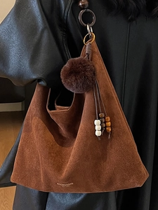 Brown suede tote bag with plush pom-poms and wooden beads on a stylish shoulder strap