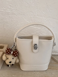Chic cream leather bucket bag with rotating metal lock and plush dog charm accessory