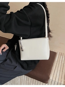 Detailed side view of a white faux leather shoulder bag with a silver chain and bean pendant