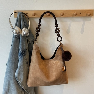 Détail d'un sac cabas en daim marron avec une poignée en perles de bois et un pendentif
