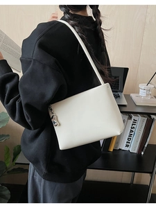 Minimalist white leather underarm bag with silver metallic pendant in a modern home office setting