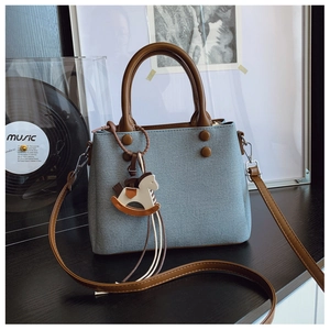 Detail of blue denim crossbody bag with brown leather handles and a horse charm