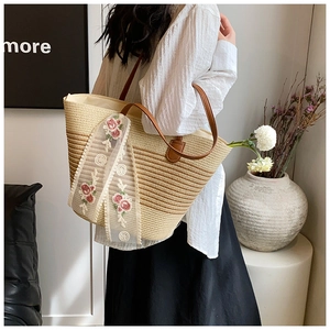 Close-up of gradient straw tote bag featuring floral lace ribbon and brown leather handles