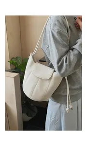 Detail of a beige lychee texture bucket bag with fine strap and metallic charms