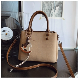 Close-up of beige fabric and brown leather crossbody bag with wooden horse charm