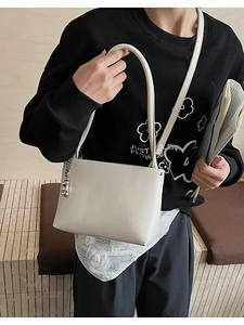 Close-up of off-white shoulder bag with silver chain detail on black sweatshirt
